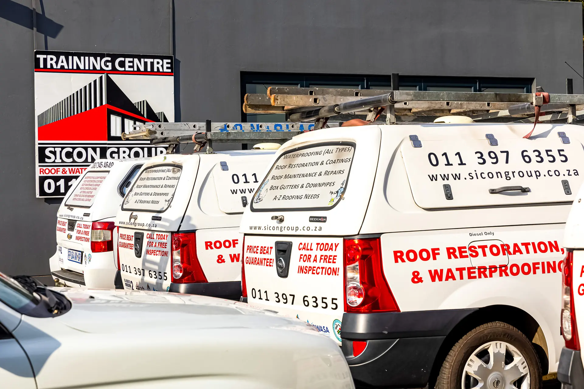 Fleet of Sicon Group white service vans with ladders parked outside their training center. Premier industrial roofing companies near me.